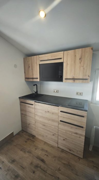 Moderne Küchenzeile mit Holzschränken und dunkler Arbeitsplatte, hellem Raum.
