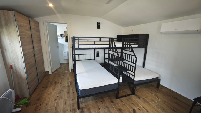 Zwei Etagenbetten in einem hellen Raum mit Holzfußboden und Schrank. 