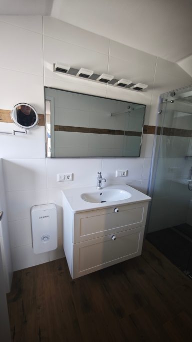 Modernes Badezimmer mit Waschbecken, Spiegelschrank und Dusche. Holzfußboden.