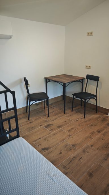 Ein einfacher Raum mit zwei schwarzen Stühlen und einem Tisch auf Holzfußboden.